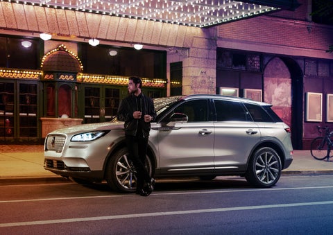 A 2022 Lincoln Corsair SUV is parked outside a theater as the driver relaxes against the frame and lights illuminate the floating roofline and body | Klaben Lincoln of Warren in Warren OH