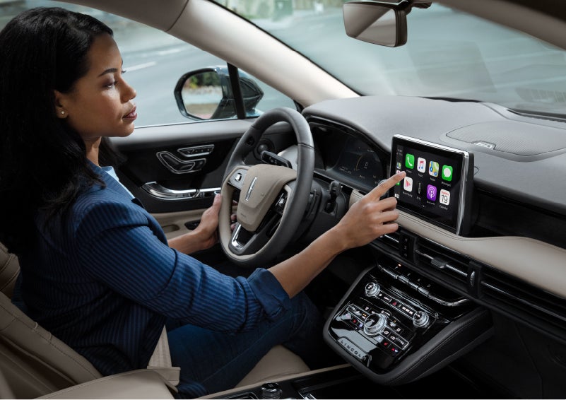 A woman in the driver’s seat of a 2022 Lincoln Corsair is touching the center digital screen to connect to Apple CarPlay<sup>®</sup> | Klaben Lincoln of Warren in Warren OH