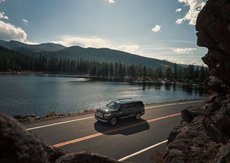 A 2022 Lincoln Navigator SUV is driving along a lake high up in the mountains | Klaben Lincoln of Warren in Warren OH