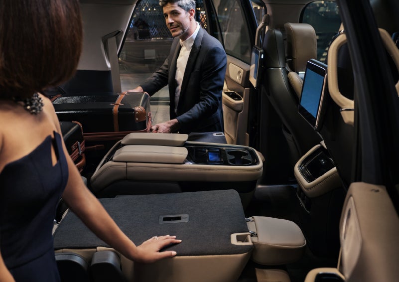 A man is pulling a suitcase out of the folded flat second-row of a 2022 Lincoln Navigator SUV | Klaben Lincoln of Warren in Warren OH