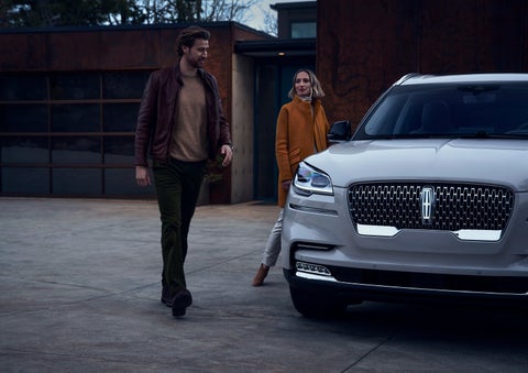 A man and a woman approaching a 2024 Lincoln Aviator® SUV, which illuminates certain lights when they are close | Klaben Lincoln of Warren in Warren OH