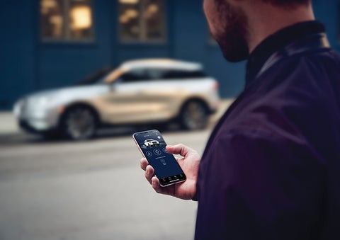 A person is shown interacting with a smartphone to connect to a Lincoln vehicle across the street. | Klaben Lincoln of Warren in Warren OH