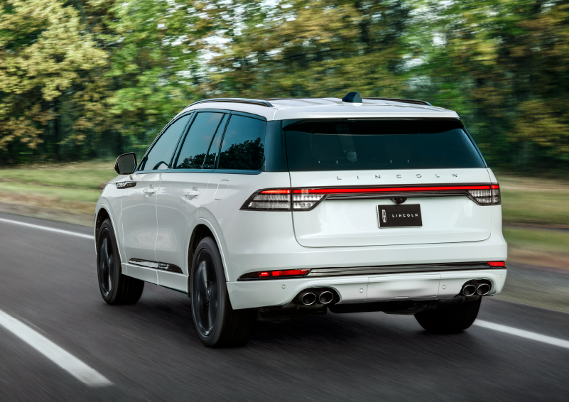 A white 2025 Lincoln Aviator® SUV is being driven away down a road lined with colorful trees. | Klaben Lincoln of Warren in Warren OH