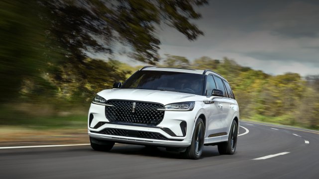 A white 2025 Lincoln Aviator® SUV is being driven down a road lined with trees. | Klaben Lincoln of Warren in Warren OH