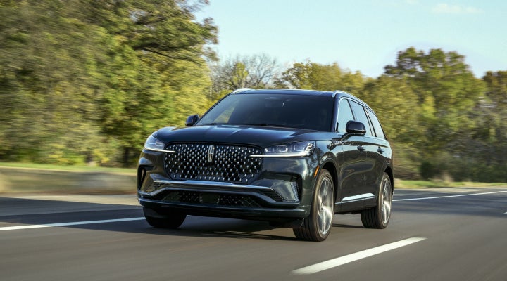 A 2026 Lincoln Black Label™ Aviator® SUV is being driven down a road lined with trees. | Klaben Lincoln of Warren in Warren OH