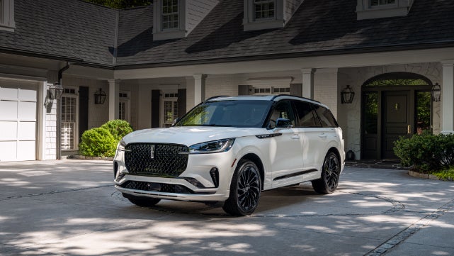 A white 2026 Lincoln Aviator® SUV is parked in the driveway of a luxury home. | Klaben Lincoln of Warren in Warren OH
