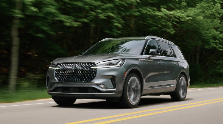 A 2027 Lincoln Aviator® SUV is being driven down a road lined with trees. | Klaben Lincoln of Warren in Warren OH